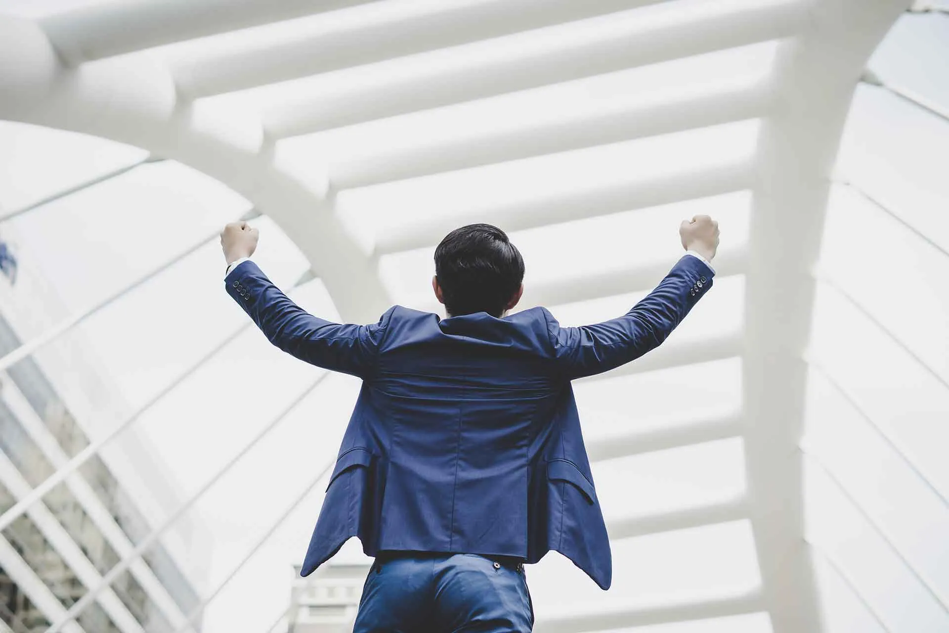 Man in a blue suit seen from behind raising both fists in triumph